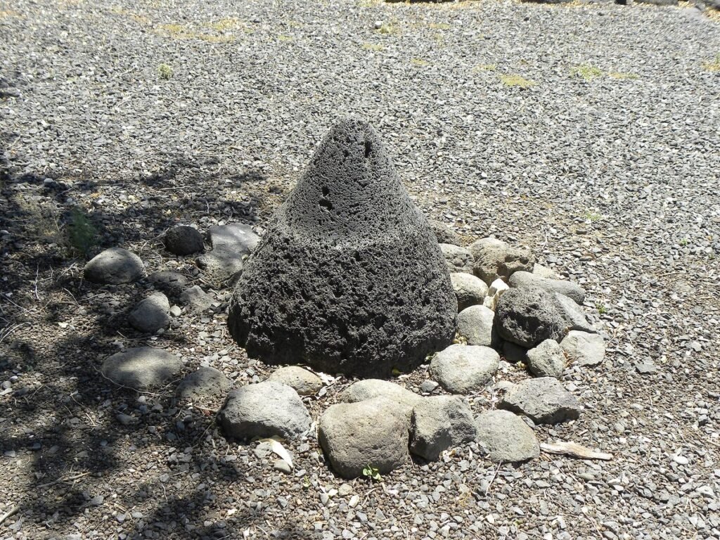 Kegelförmiger Mühlstein aus schwarzem Basalt zwischen Steinen