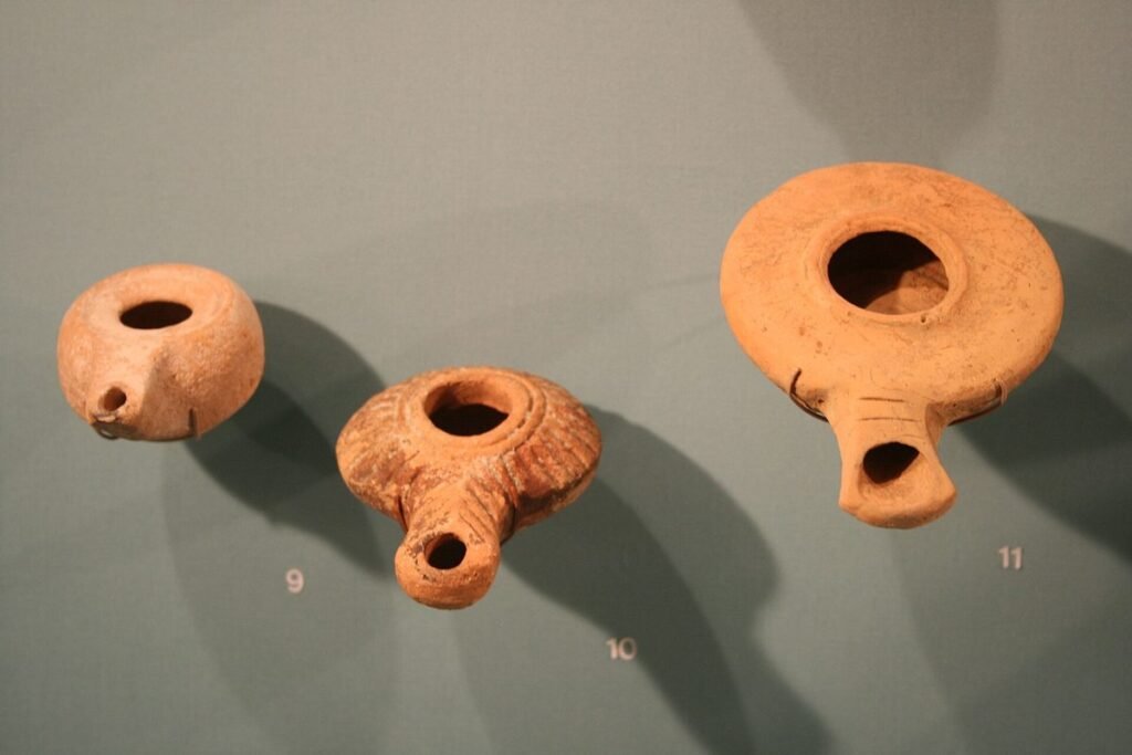 Drei kleine Öllampen aus rötlichem Ton an einer Museumswand