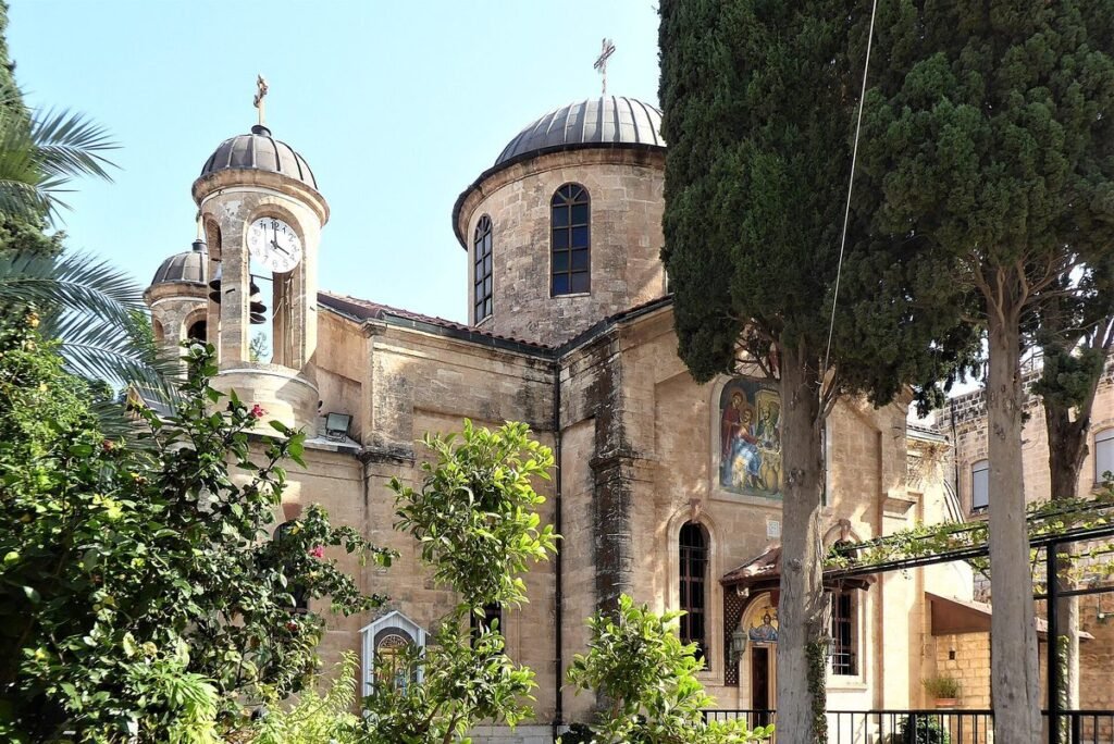 Kirche mit Kuppeln und Glockenturm zwischen Zypressen in Kafr Kanna