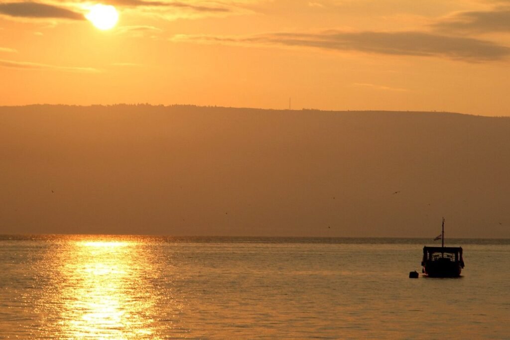 Die Sonne geht über den Hügeln am See von Galiläa auf, ein Boot liegt auf dem Wasser